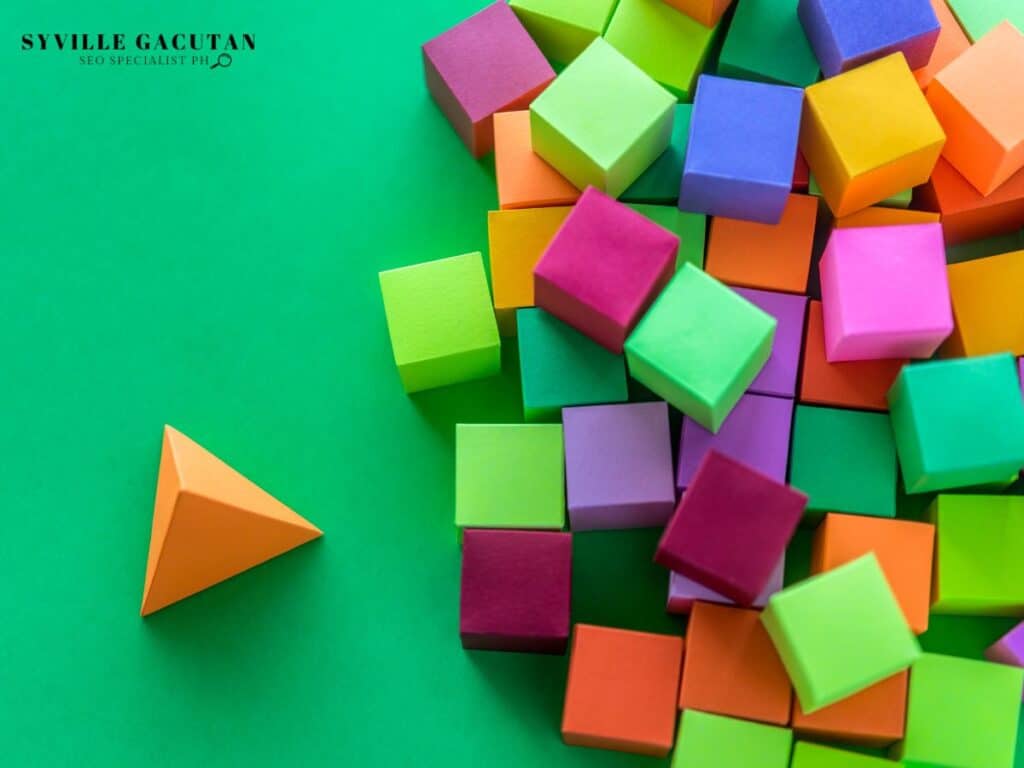 Colorful geometric shapes - orange triangle and multicolored cubes on green background.