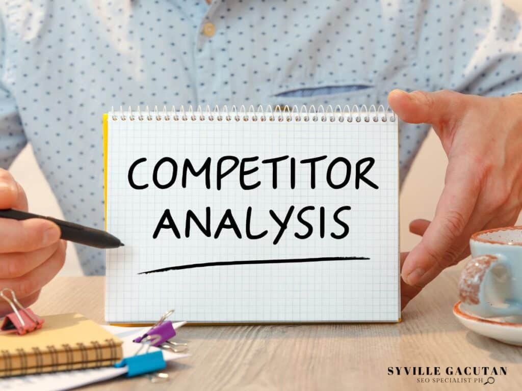 Notepad showing "Competitor Analysis" text with office supplies and polka dot fabric in background.