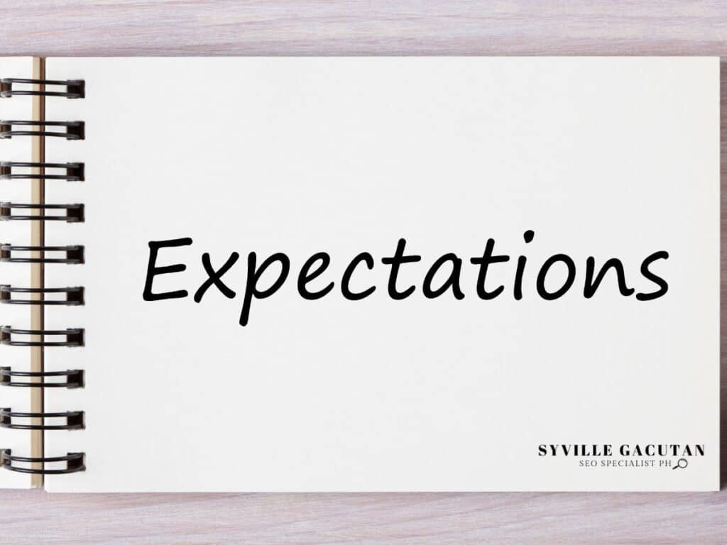 Spiral notebook showing "Expectations" text in black handwriting on white page.