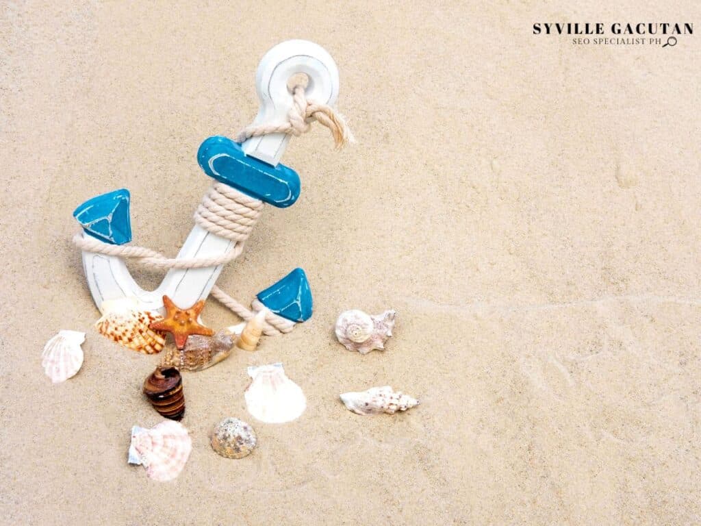 Decorative white and blue anchor with seashells and starfish on sandy beach background.