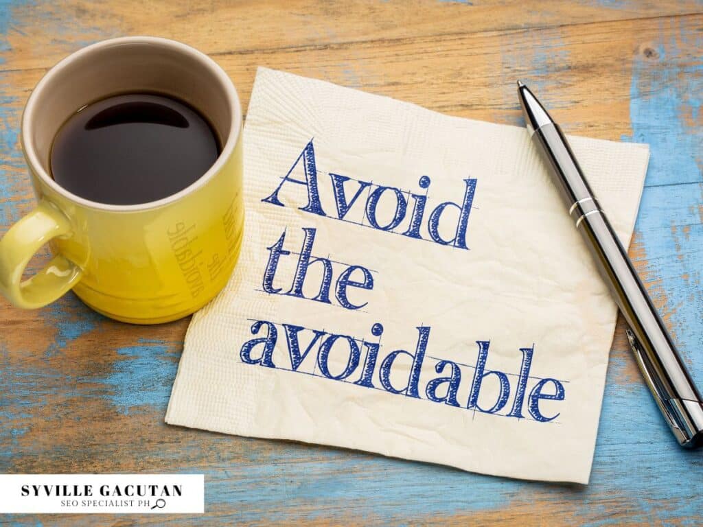 Yellow mug with coffee, napkin saying "Avoid the avoidable", pen on weathered wooden surface.