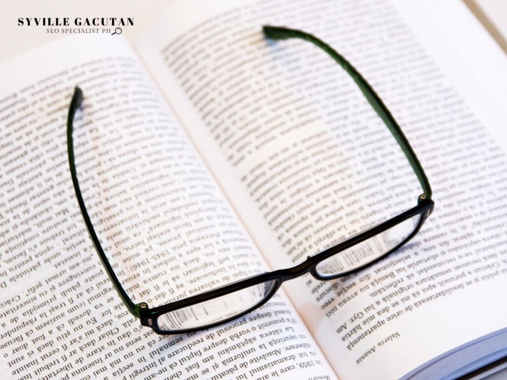 Reading glasses resting on an open book with dense text visible on its pages.