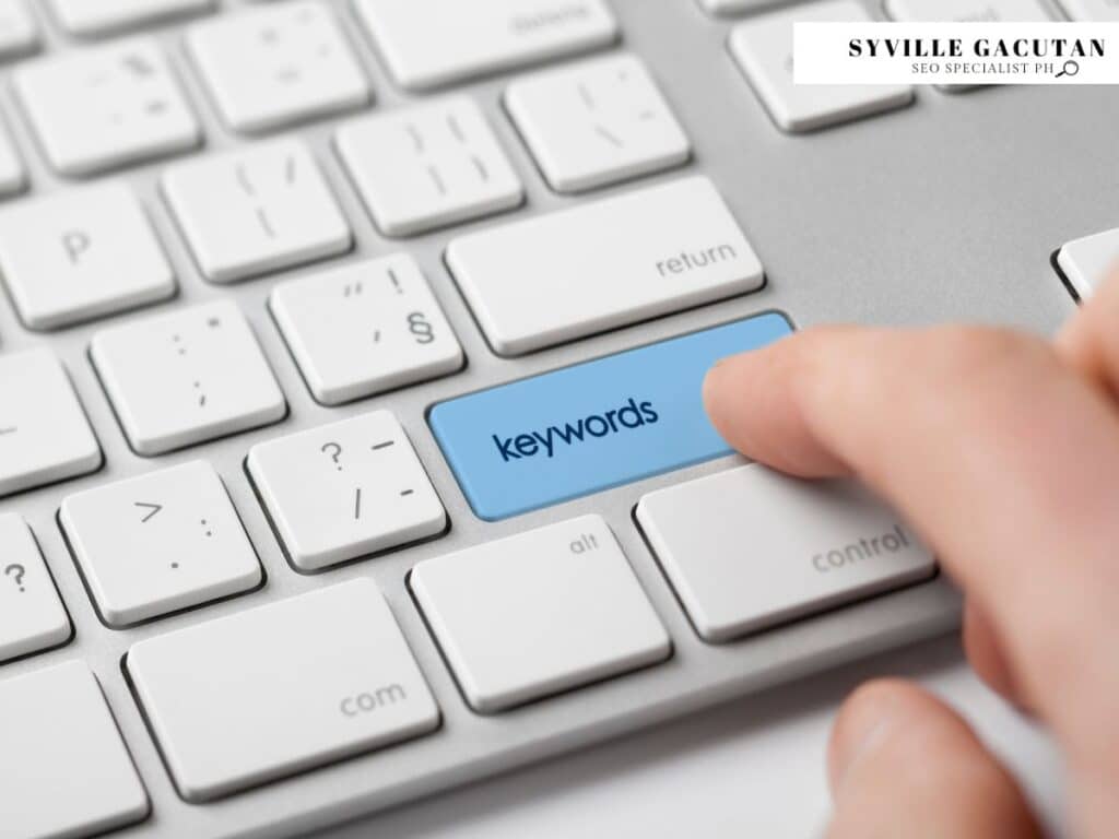 A close-up of a keyboard with a blue "keywords" key being pressed by a finger.