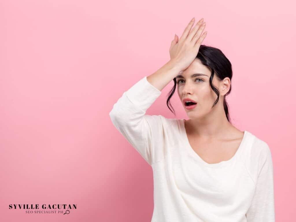 Woman in white top showing frustration gesture against pink background.