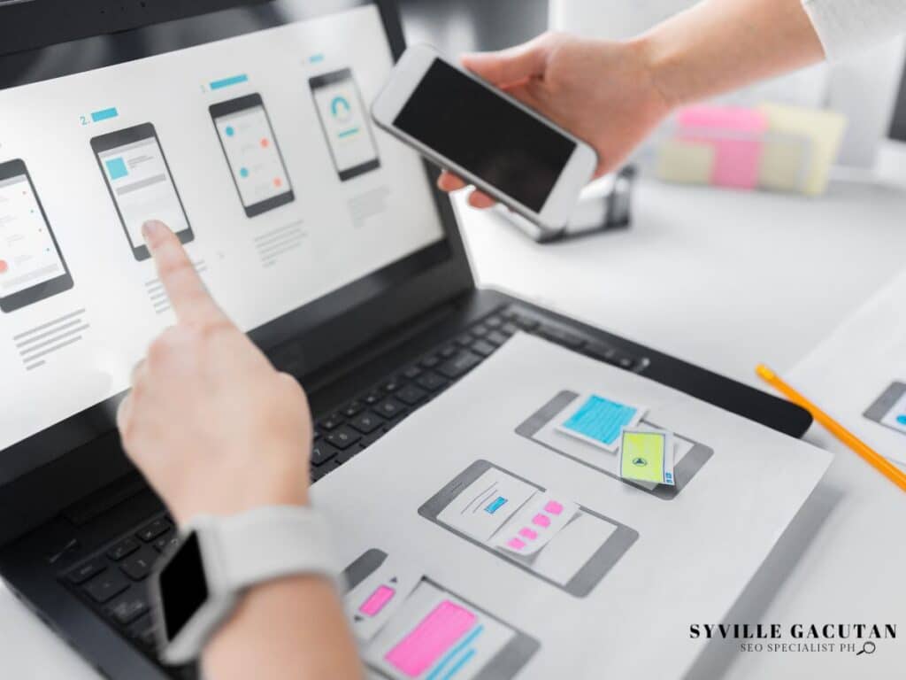 Hands pointing at a phone interface design on a laptop screen.