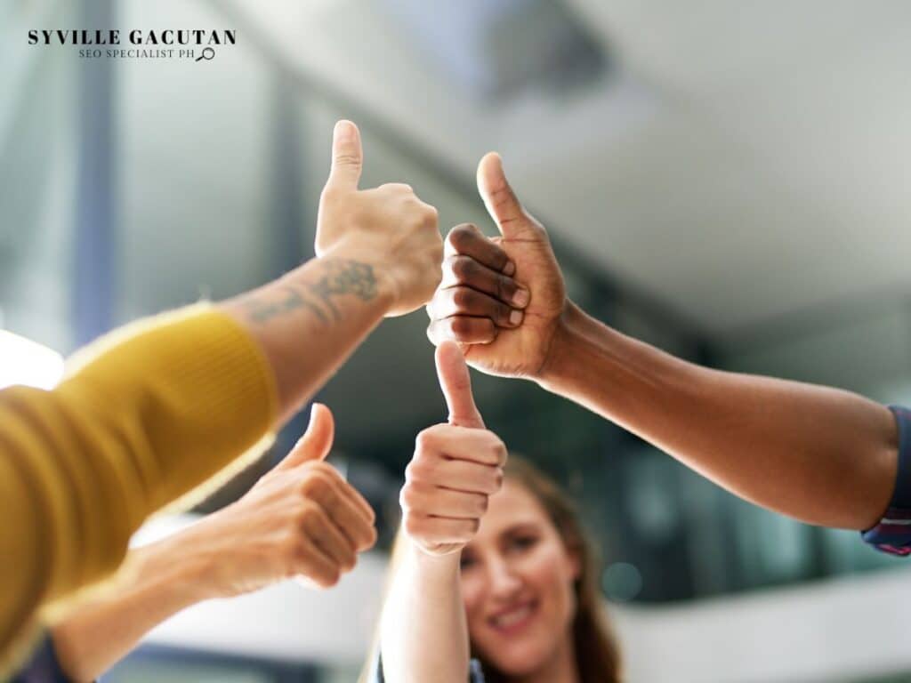 Multiple hands showing thumbs up in unity, with yellow sleeve and tattoo visible.