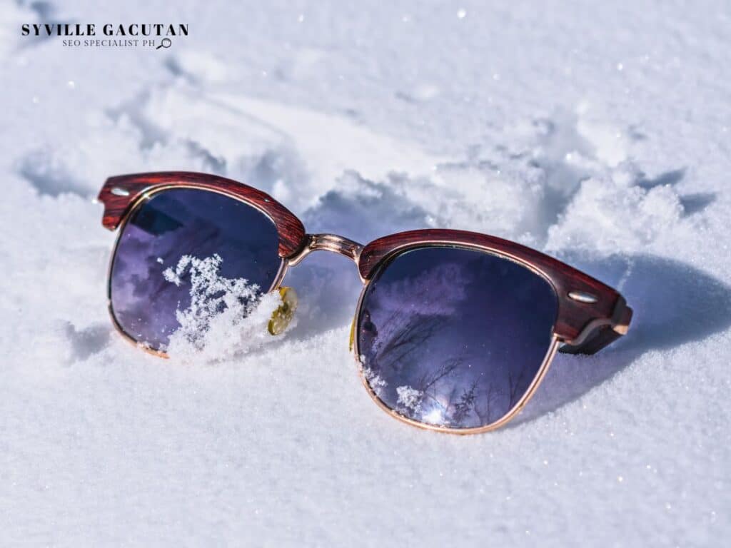 Brown clubmaster sunglasses lying on fresh white snow with delicate snowflakes.