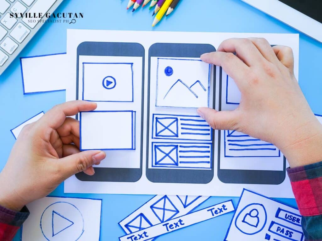 Hands arranging mobile app wireframes with blue sketches on white paper.