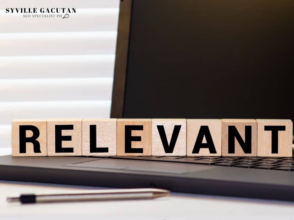 Wooden letter blocks spelling "RELEVANT" placed on laptop keyboard with pen nearby.