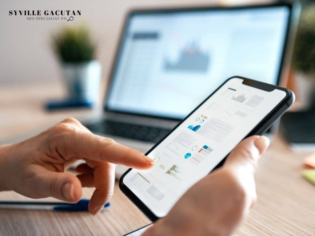 Hands using smartphone showing analytics data with laptop in background.