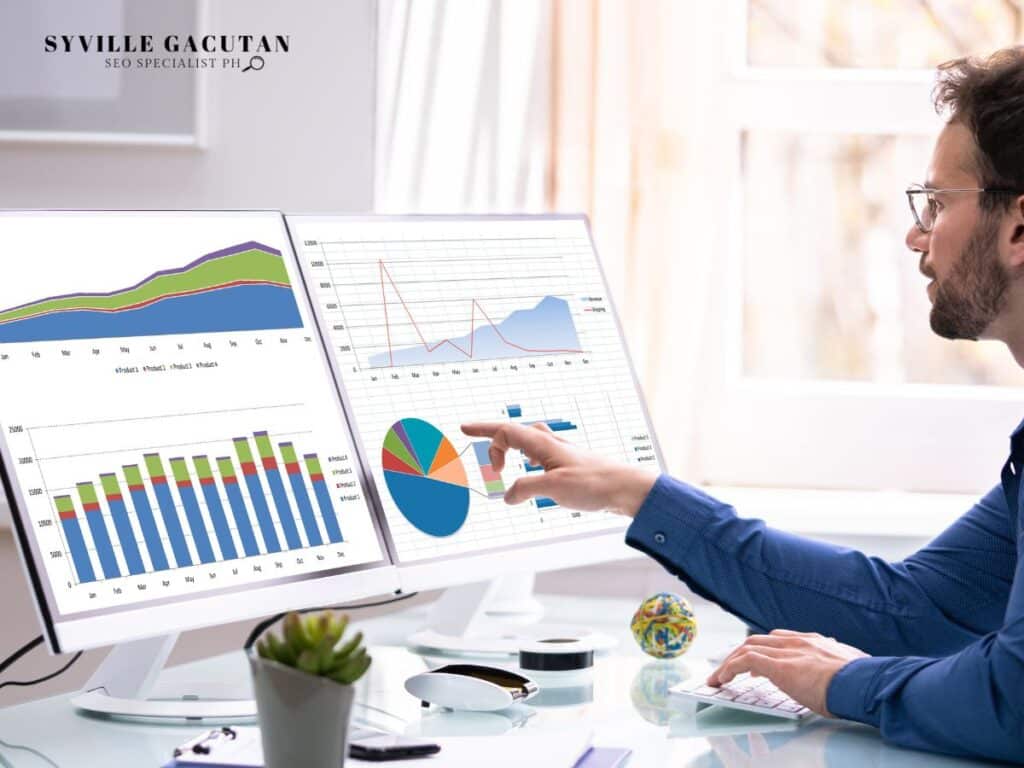 A man analyzing colorful business charts and graphs on dual monitors with succulent plant on desk.