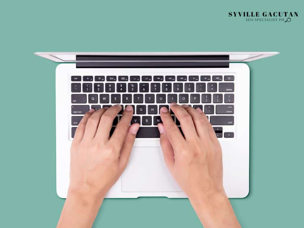 Hands typing on white laptop keyboard against mint green background.