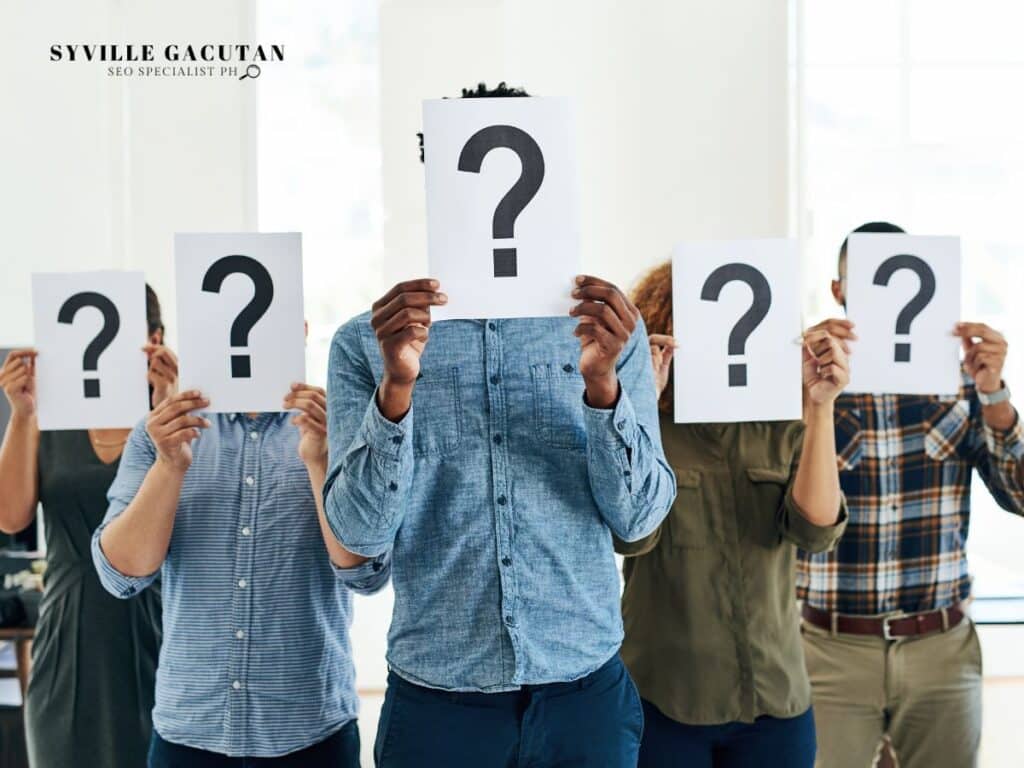 Group of people holding question mark signs covering their faces.