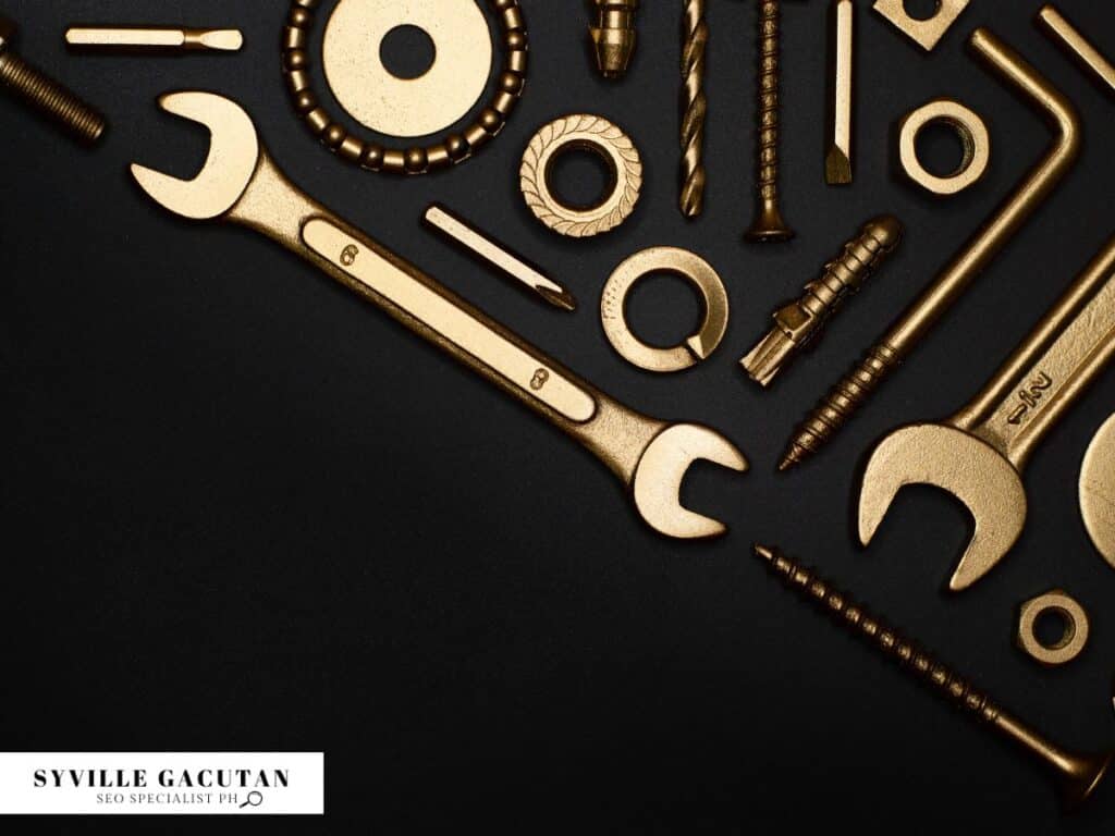 Golden tools and hardware arranged on black background, including wrenches and screws.