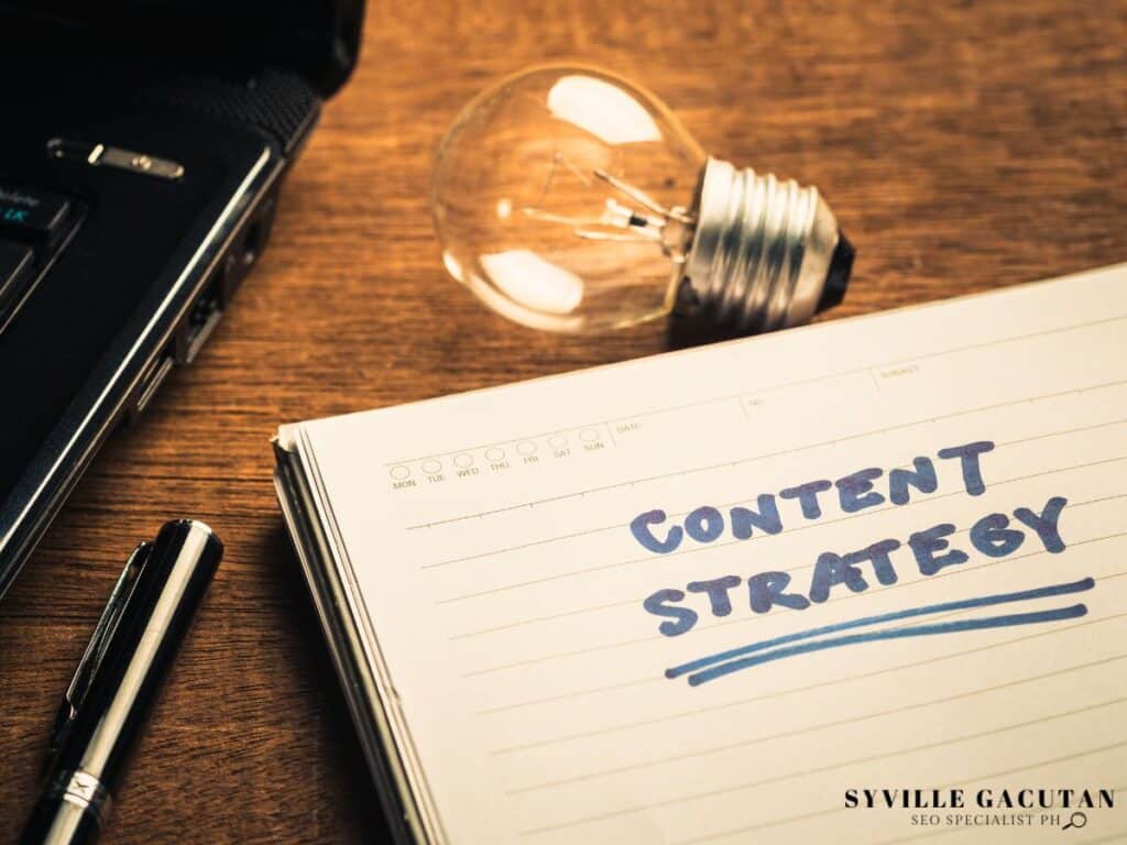 Notebook with "Content Strategy" text beside lightbulb and laptop on wooden desk.