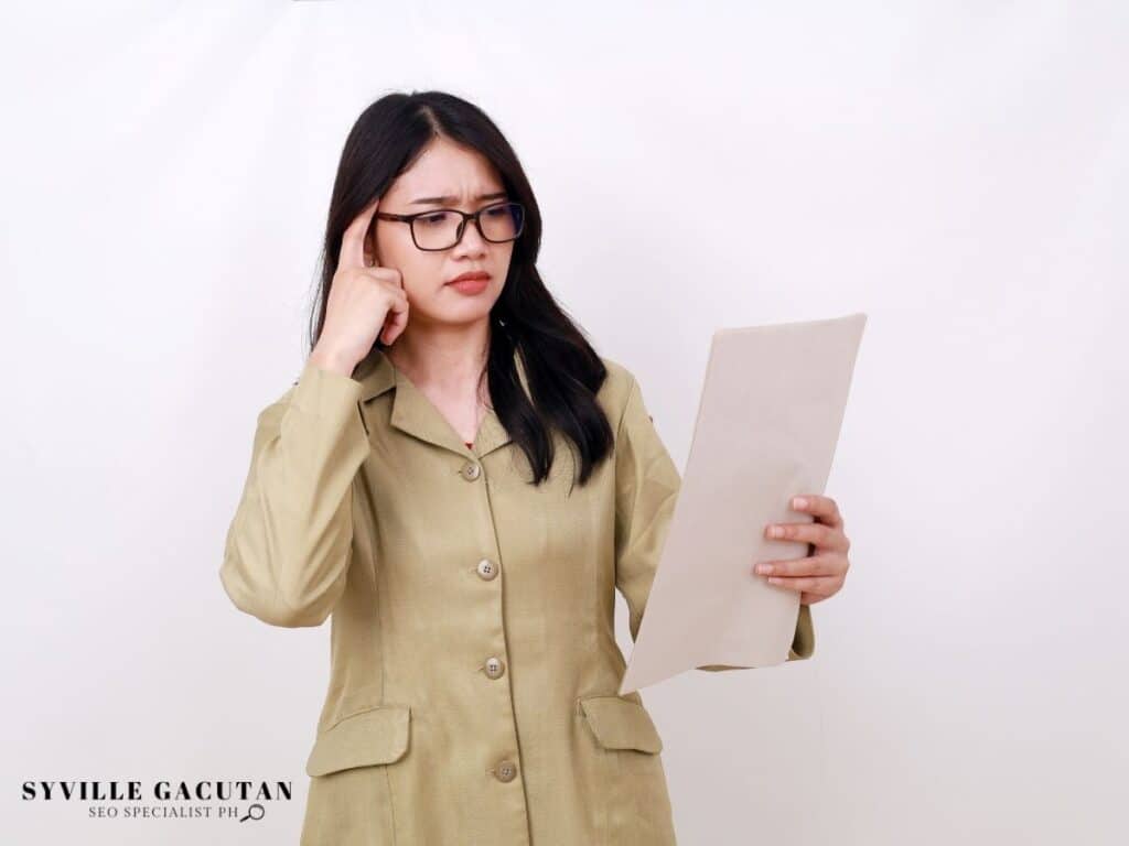 Professional in beige blazer reviewing document with concerned expression against white background.