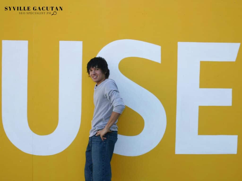 Person in casual wear leaning against large white "USE" text on yellow wall.
