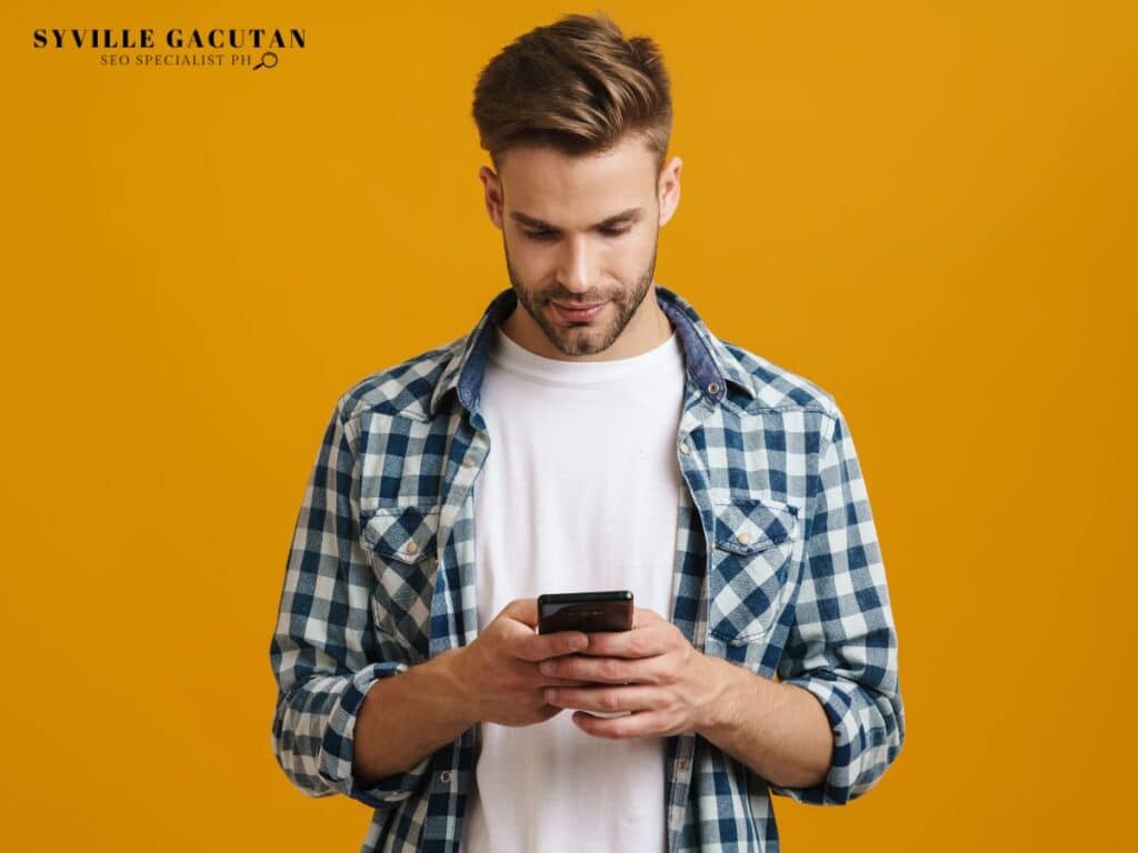 Man in a checkered shirt using a smartphone against a yellow background.