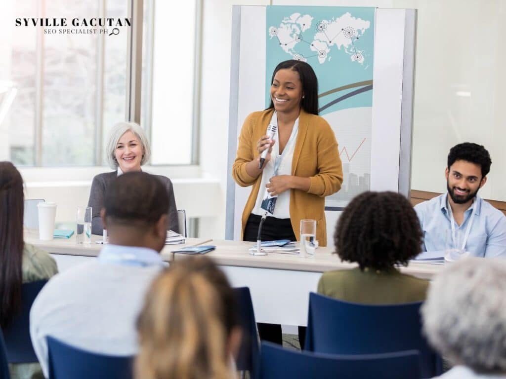 Woman speaking at a panel with smiling audience and charts.

