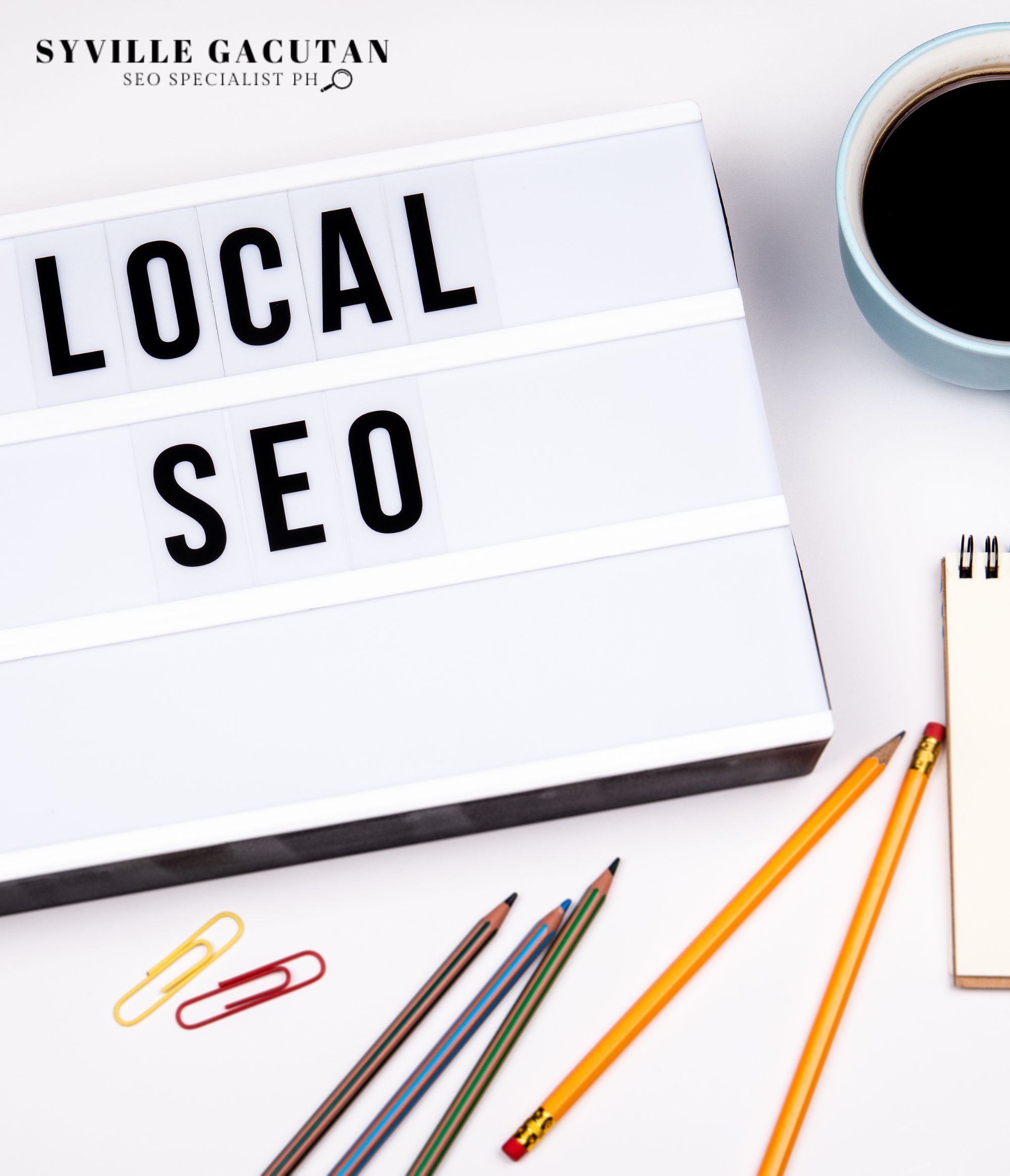 Lightbox sign displaying "LOCAL SEO" with coffee cup, pencils, and paperclips on white surface.