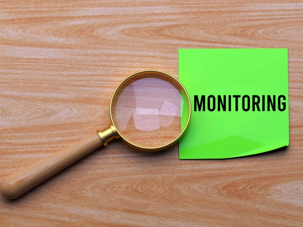 Magnifying glass beside a green note labeled “MONITORING” on wood.