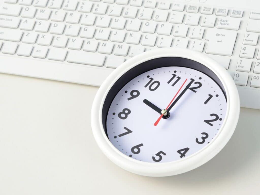 Desk clock beside keyboard showing time management concept.