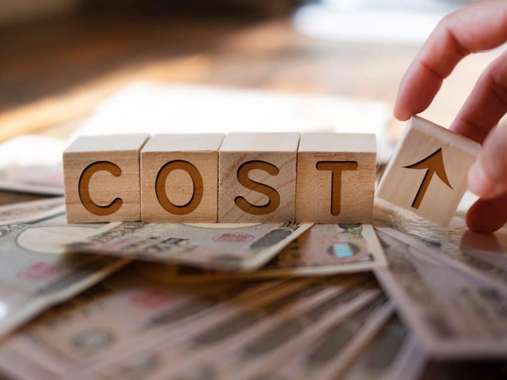 Wooden blocks spelling “Cost” with upward arrow over money.