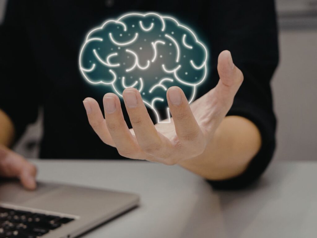Hand holding a glowing brain icon near a laptop.