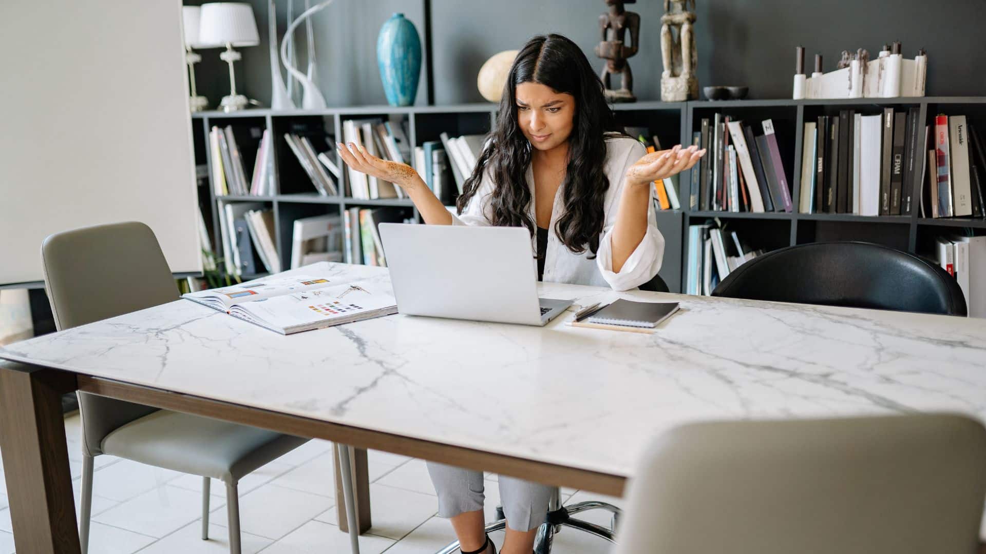 Woman looking confused while working on a laptop at a large desk.