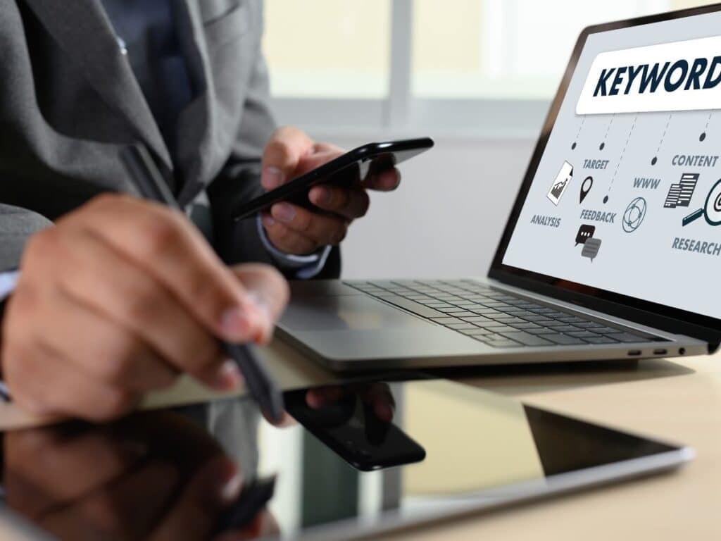 Person using phone and laptop with keyword research graphics on screen.