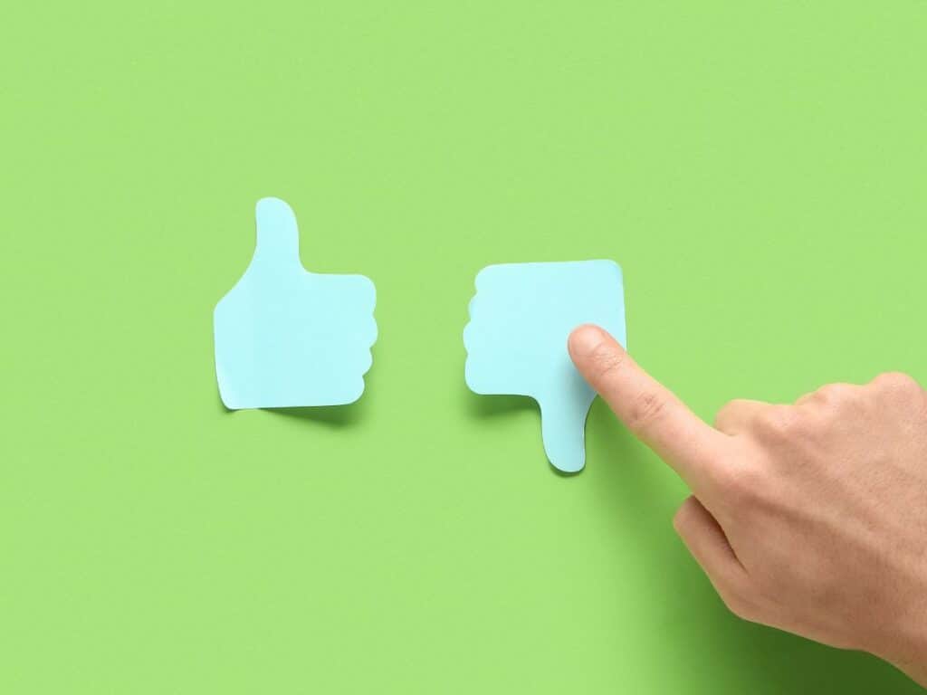 Hand pointing at a thumbs-down icon beside a thumbs-up symbol.