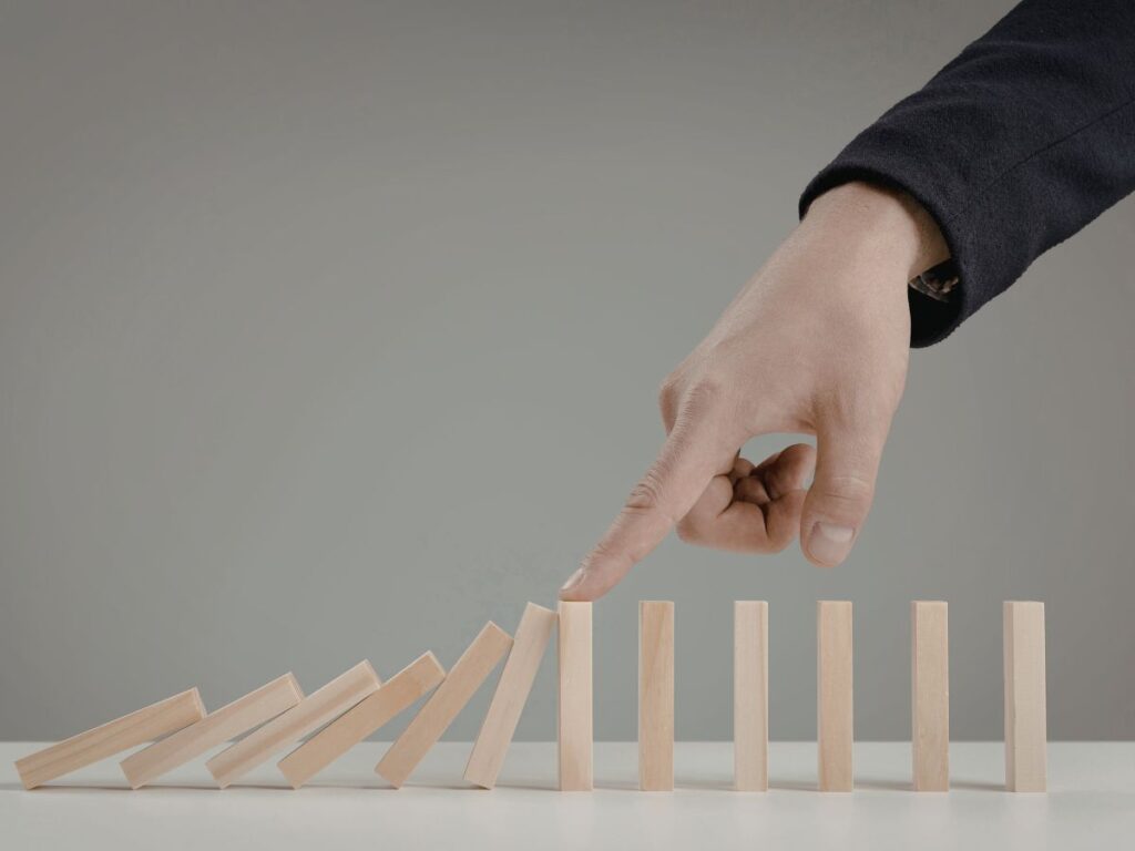 Hand stopping falling domino blocks.