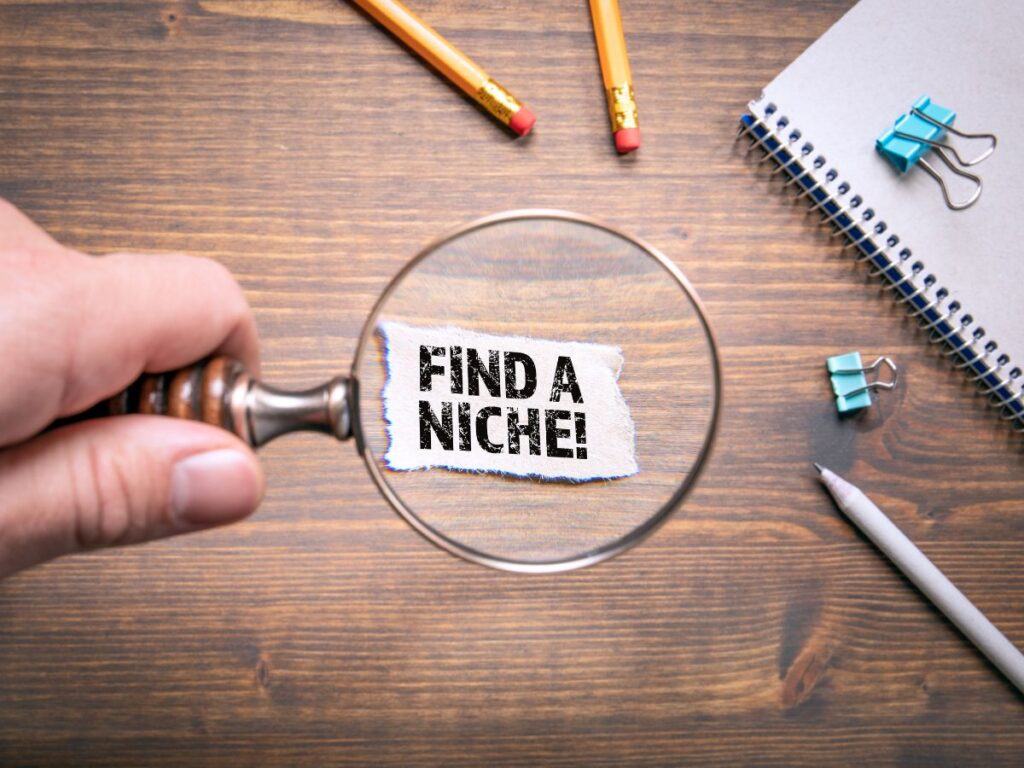 Magnifying glass highlighting “Find a Niche!” on a desk.