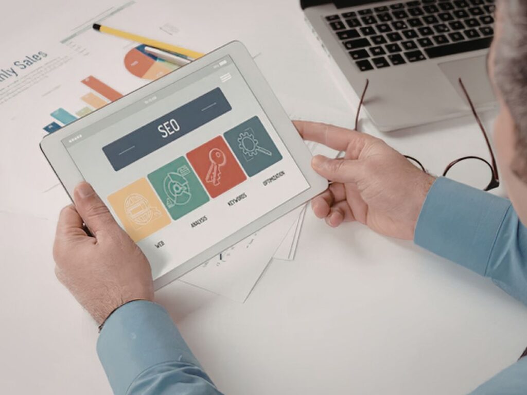 Tablet showing SEO icons and charts on a desk workspace.