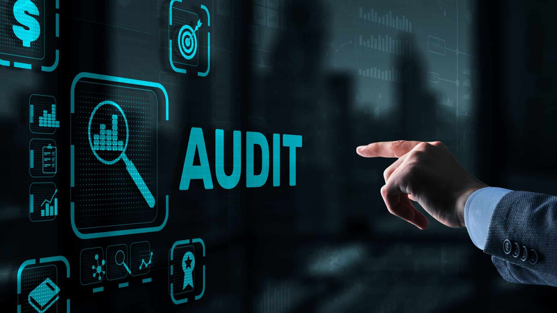 Hand pointing at a digital screen displaying the word “AUDIT” and analytics icons.