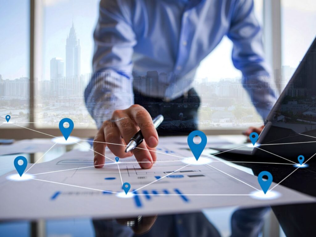 Person reviewing location data and maps on documents beside a laptop.