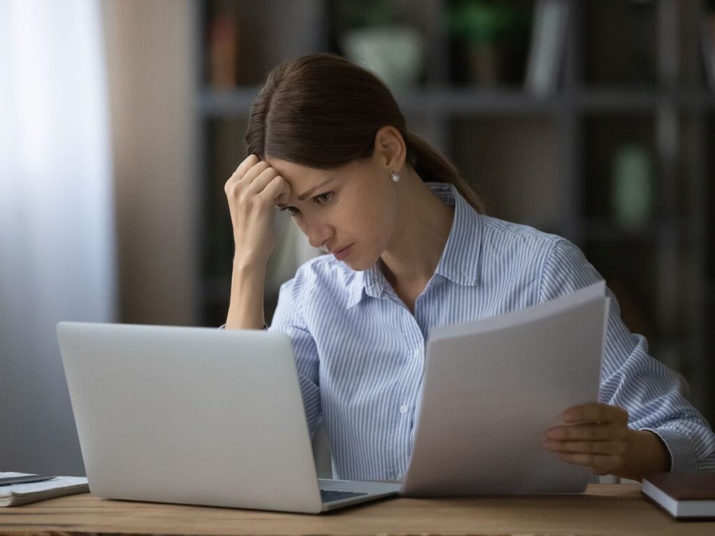 Woman reviewing papers beside a laptop.