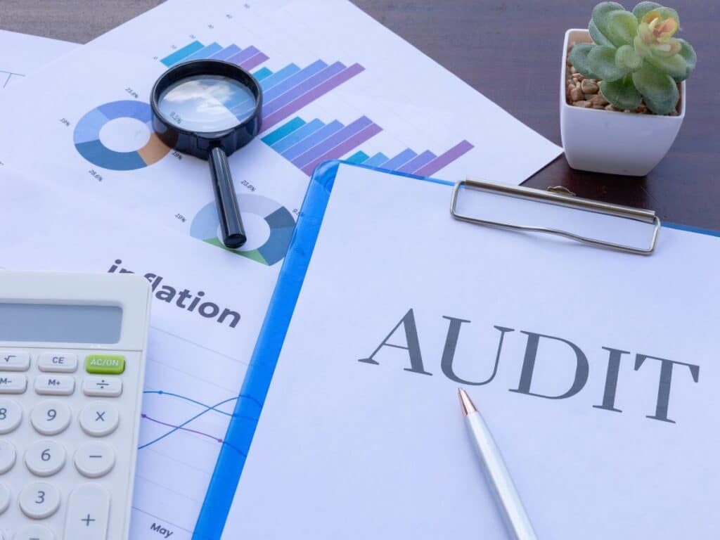 Audit document with charts, magnifier, calculator, and pen on desk.