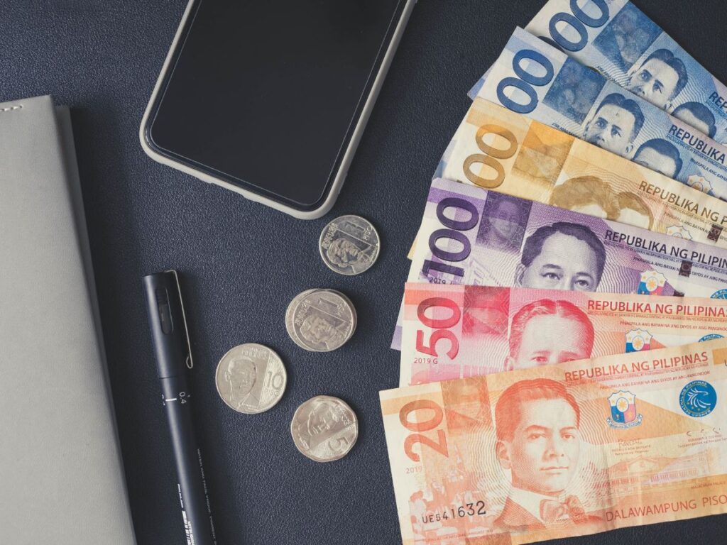 Philippine peso bills and coins beside office essentials